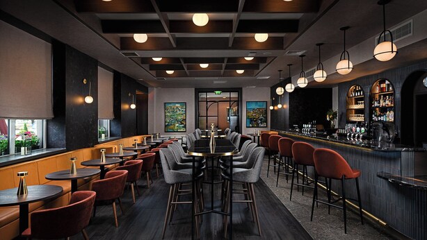 Zona de bar moderna con diversas opciones de asientos, incluyendo taburetes y mesas, y una barra con una variedad de botellas.