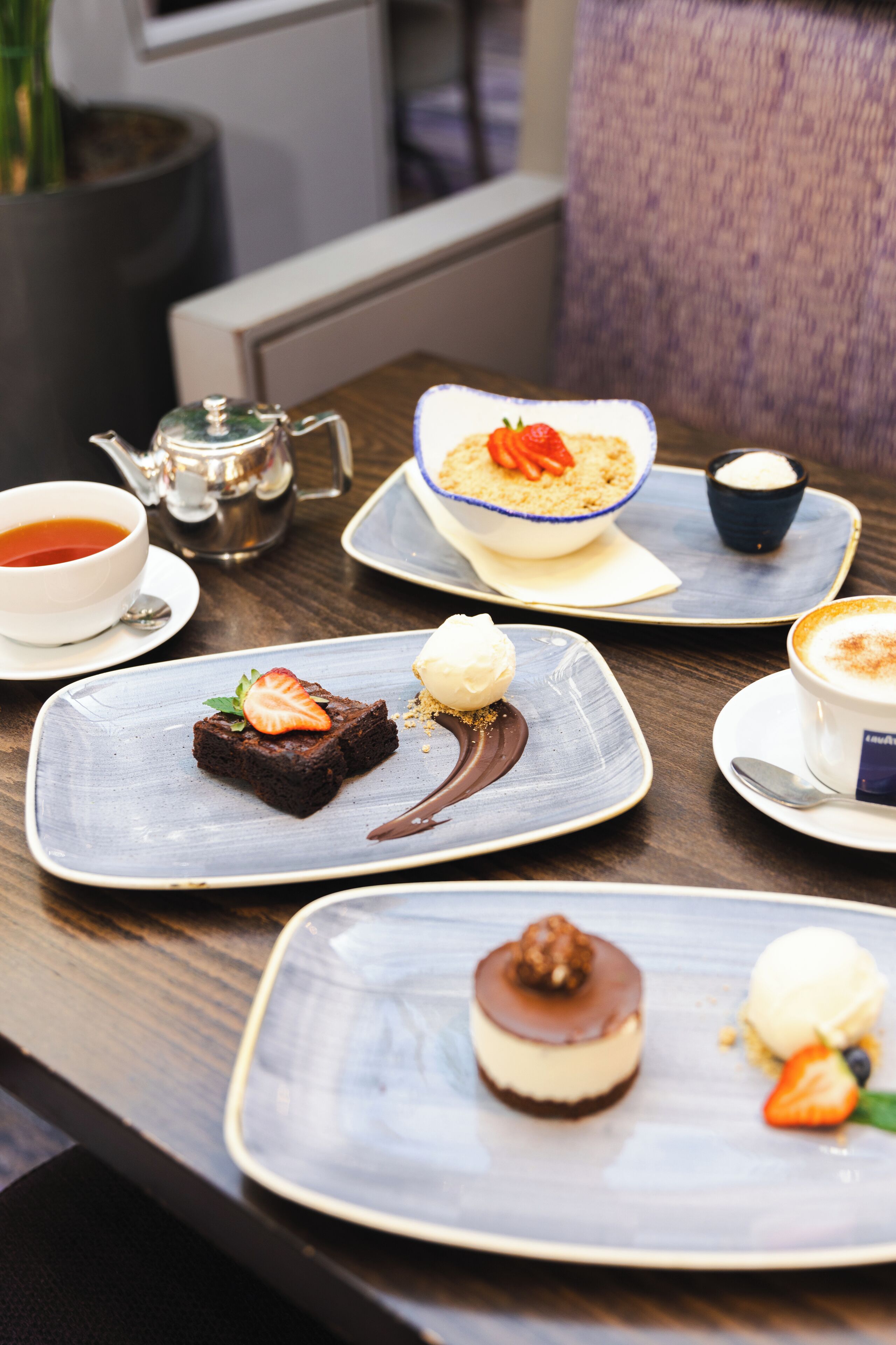 A table with various desserts and a teapot, suggesting a dining setting.
