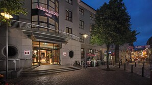 Fachada de hotel con diseño moderno, una escalera visible y vista a la calle con comercios.
