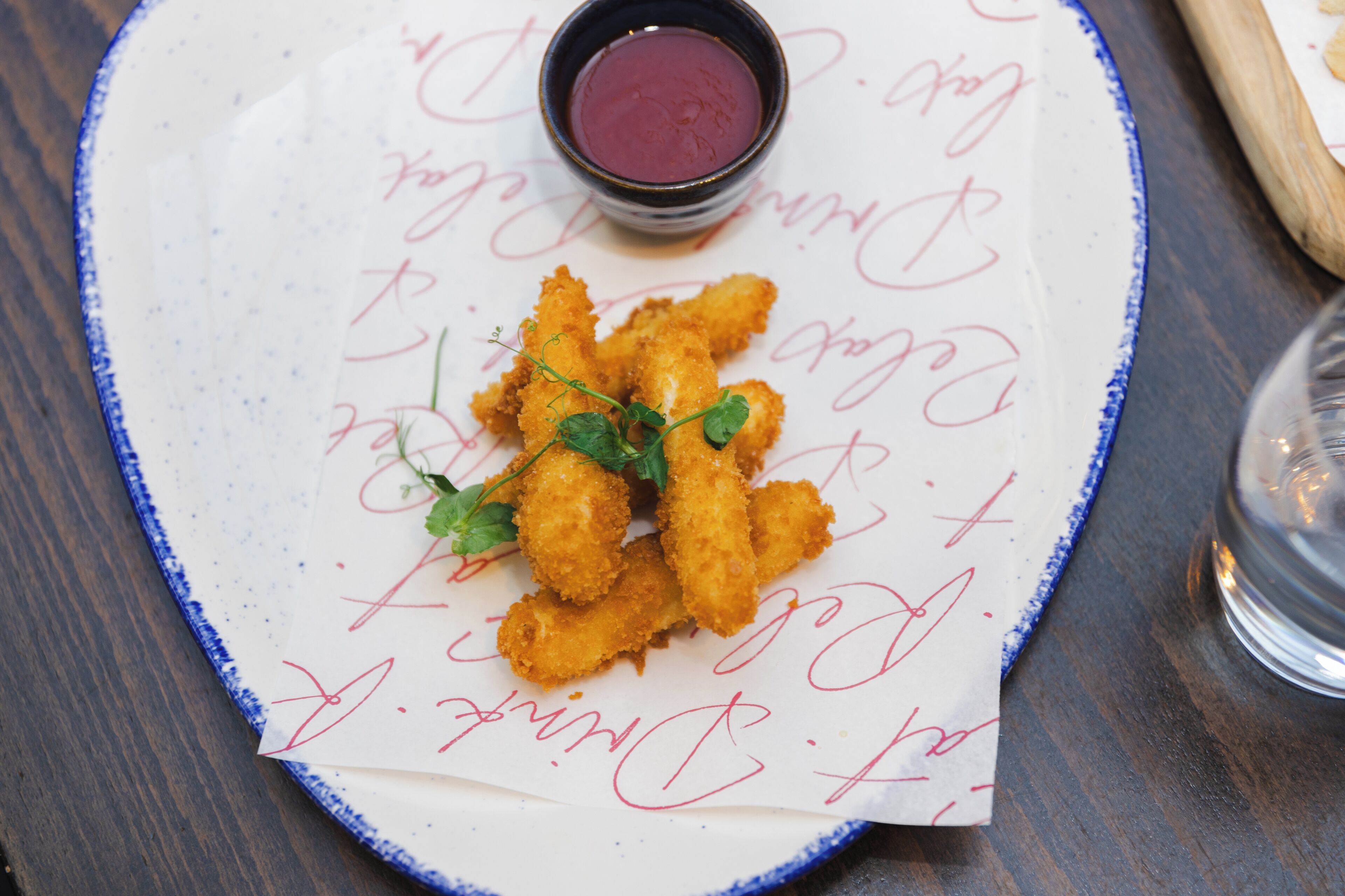 Un plato de comida rebozada y frita, adornado con hierbas, acompañado de una pequeña cazuela de salsa para mojar.