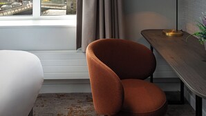 Una habitació d'hotel moderna amb un gran finestral, un escriptori de fusta, una cadira marró i un llit blanc.