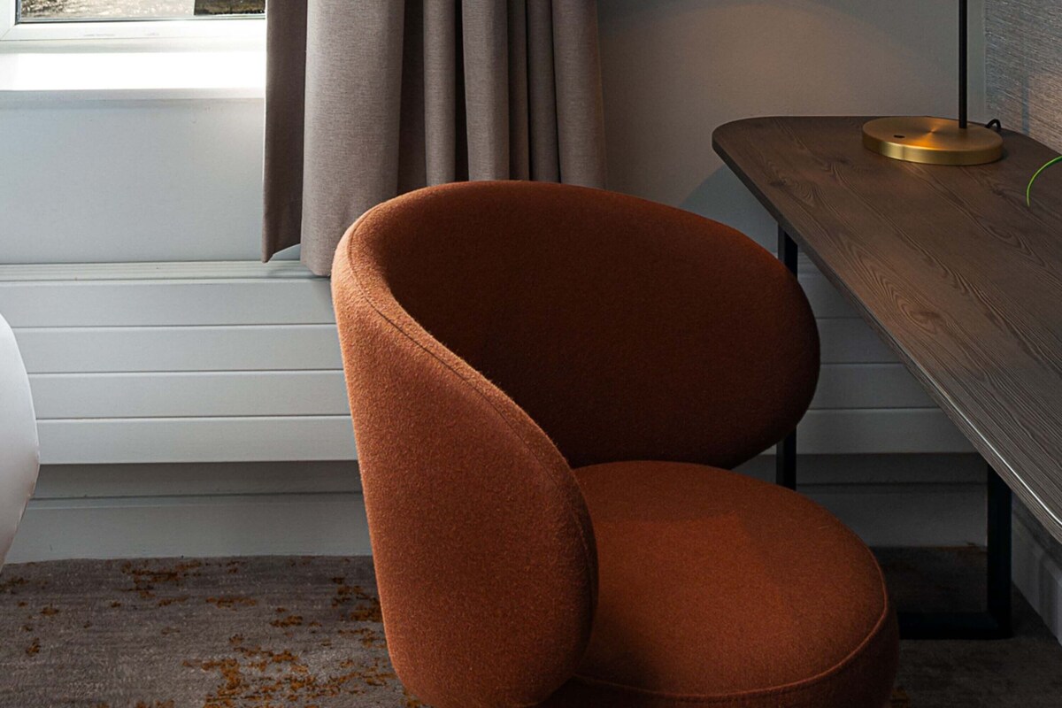 A modern room with a brown upholstered chair, a wooden table with a green object on it, and a window with curtains.