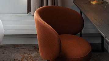 Una habitación moderna con una butaca tapizada de color marrón, una mesa de madera con un objeto verde encima y una ventana con cortinas.