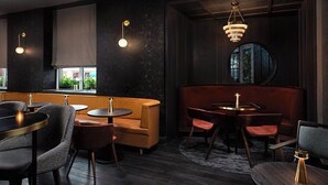 Un interior de restaurante moderno con paredes oscuras, mesas redondas y asientos acolchados.