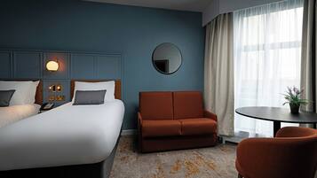 A hotel room with a bed, a sofa, a chair, a small table, a mirror, and a window with curtains.