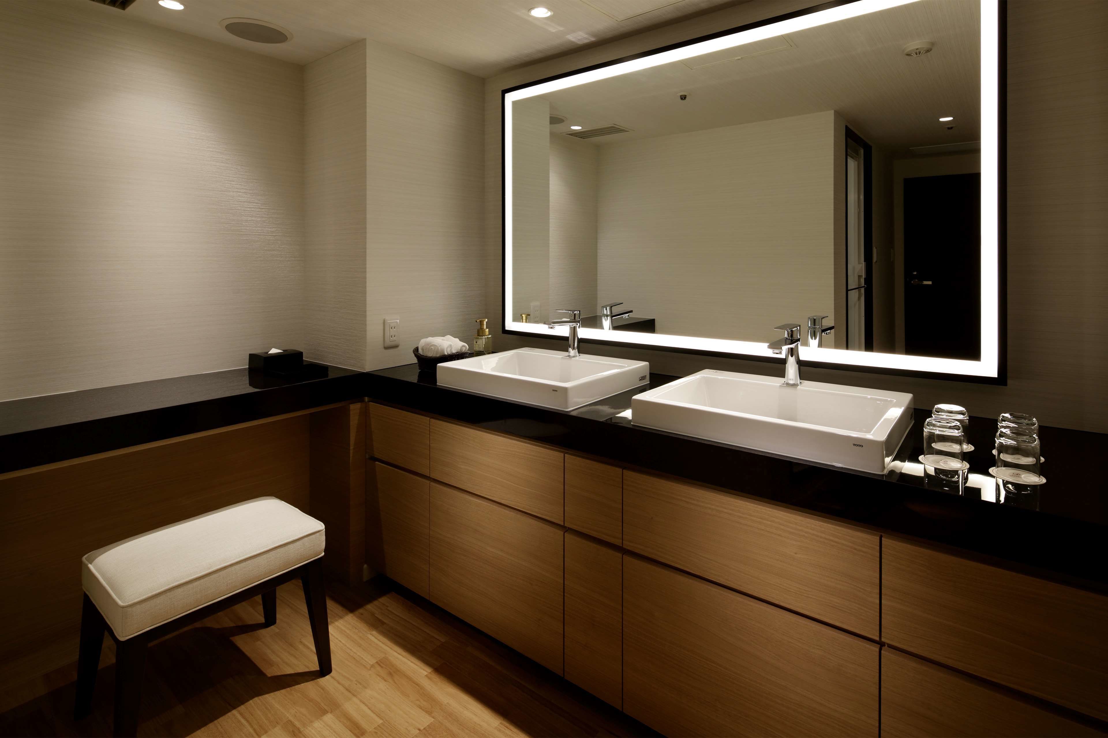 A modern bathroom with two sinks, a bench, and a large mirror.