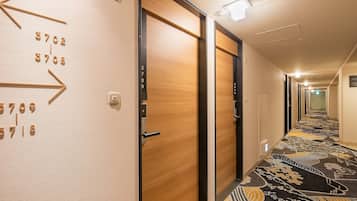 A hotel hallway with numbered doors, a patterned carpet, and a modern light fixture.