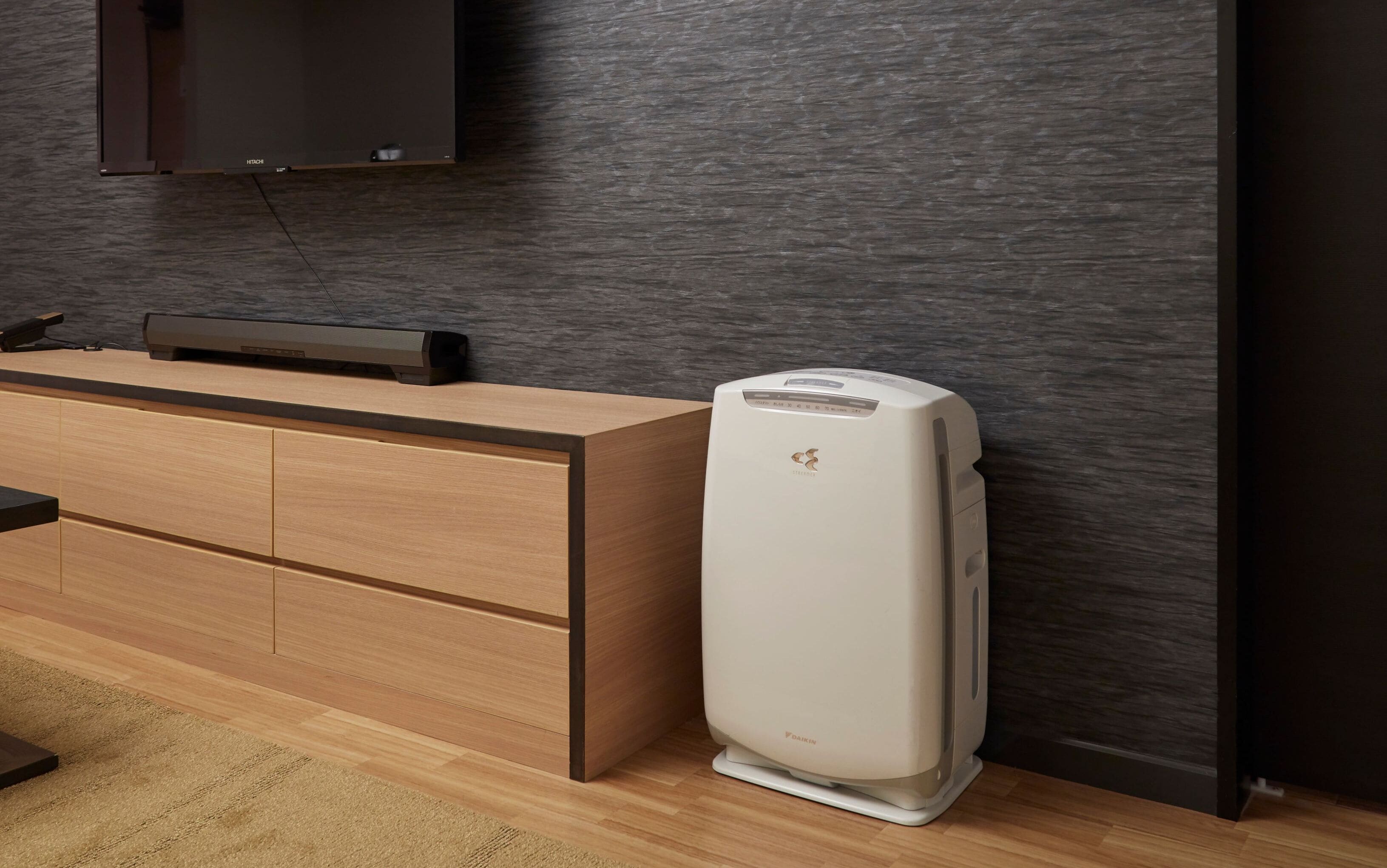 A modern room with a wooden desk, a flat-screen TV mounted on the wall, and a white air purifier on the floor.