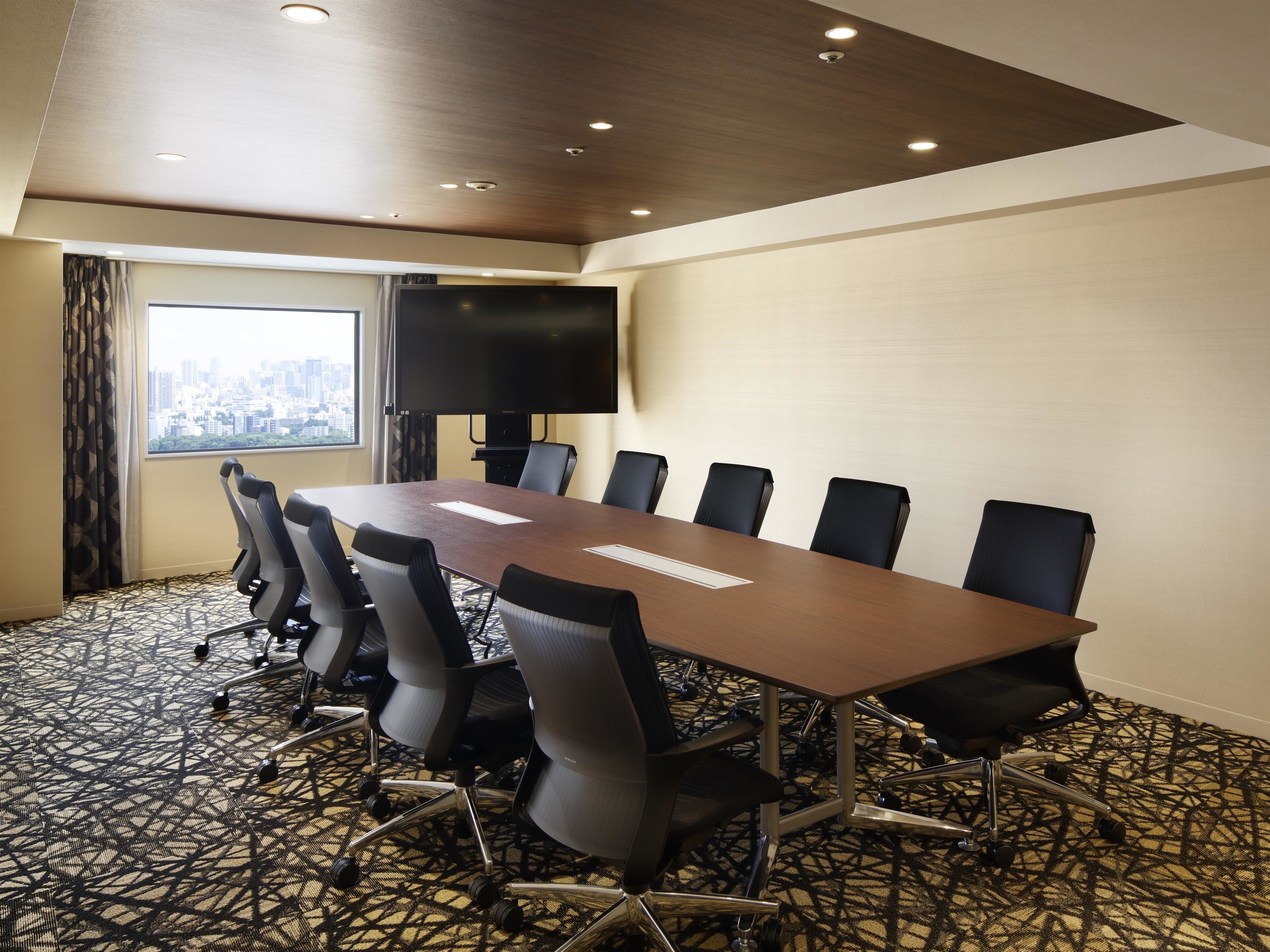 Une salle de conférence équipée d’une longue table, de six chaises, d’un téléviseur à écran plat et offrant une vue sur la ville par une fenêtre.