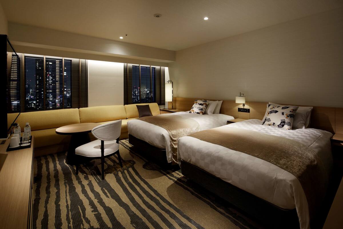 A hotel room with two beds, a sofa, a small table, and a chair.