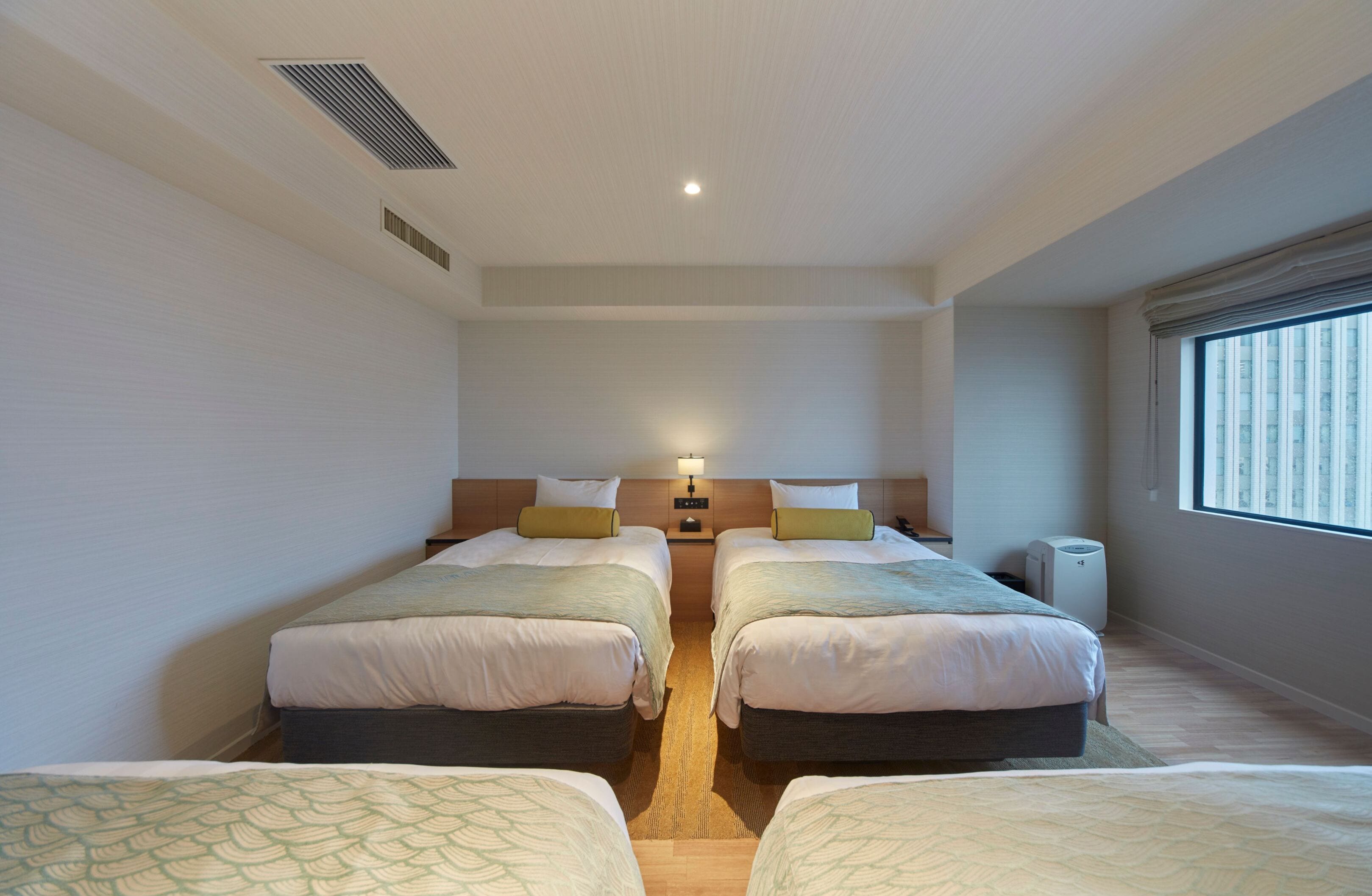 Habitación de hotel con dos camas, una mesita de noche, una lámpara, un calentador y una ventana con persianas.