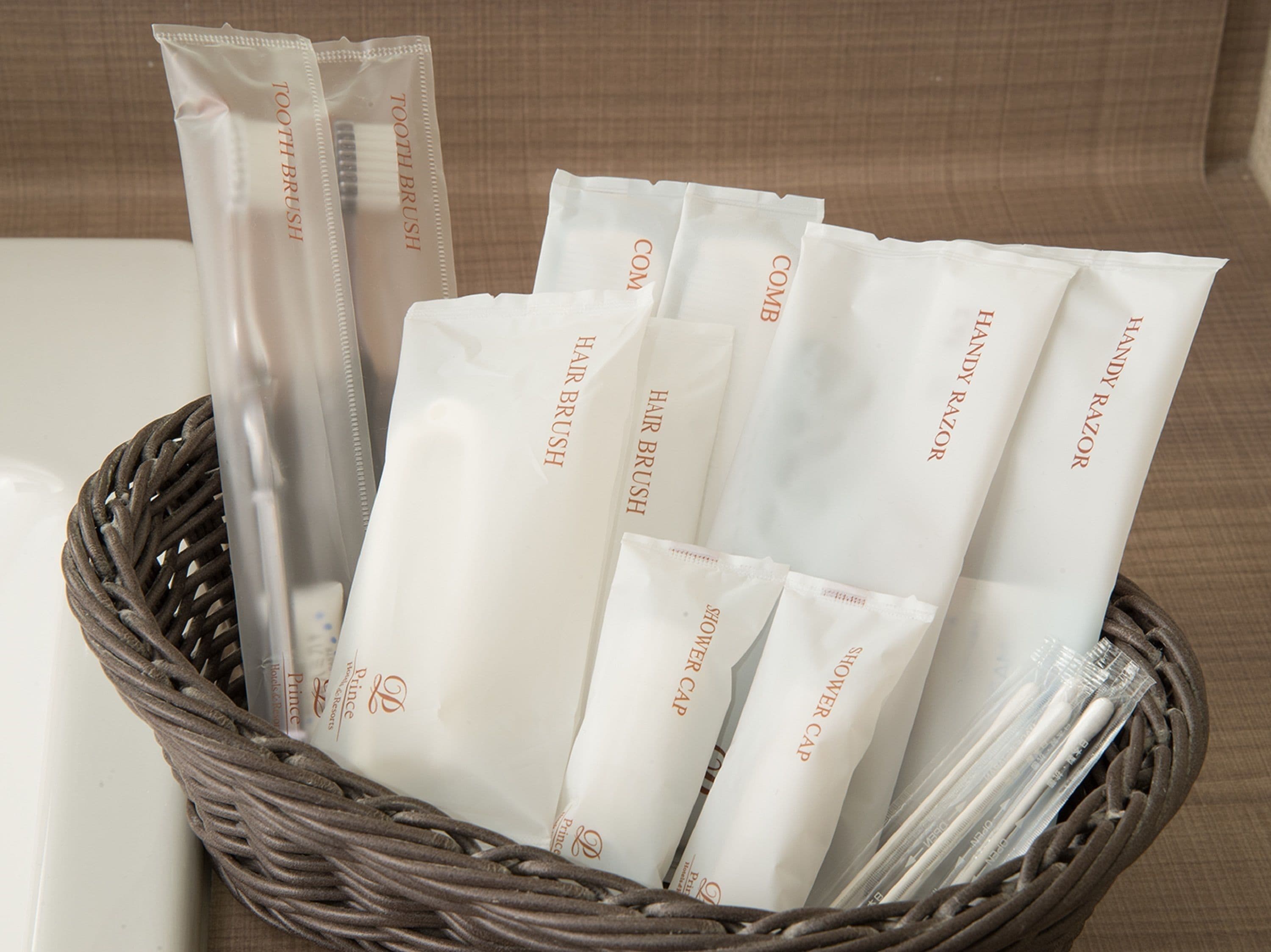 A wicker basket containing various toiletries including toothbrushes, hairbrushes, razors, and shower caps.