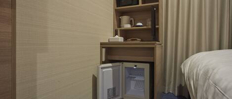 A compact hotel room with a built-in minibar, a small refrigerator, a microwave, and a bedside table with a lamp.