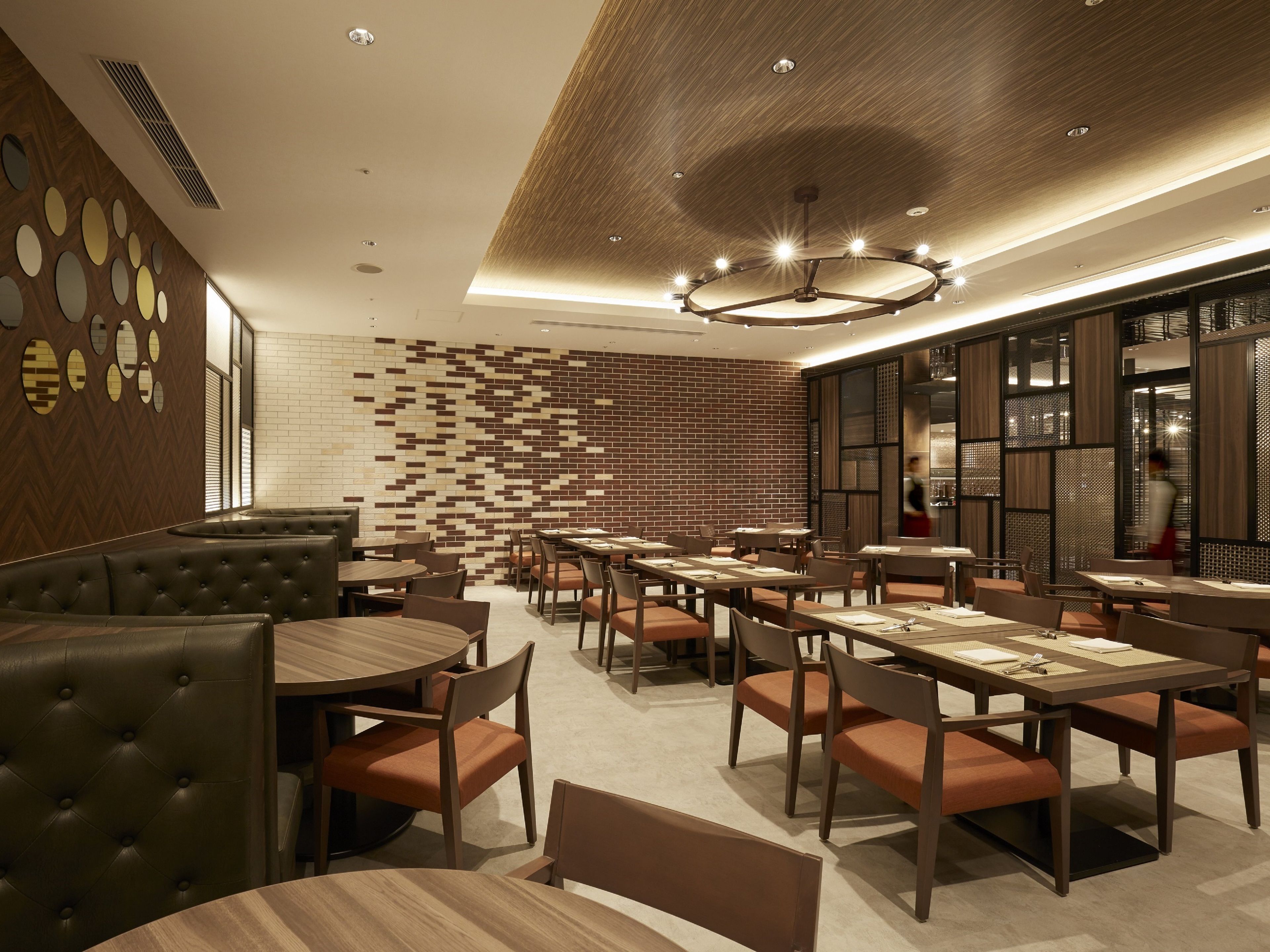A modern restaurant interior with round tables, cushioned booths, and a patterned brick wall.