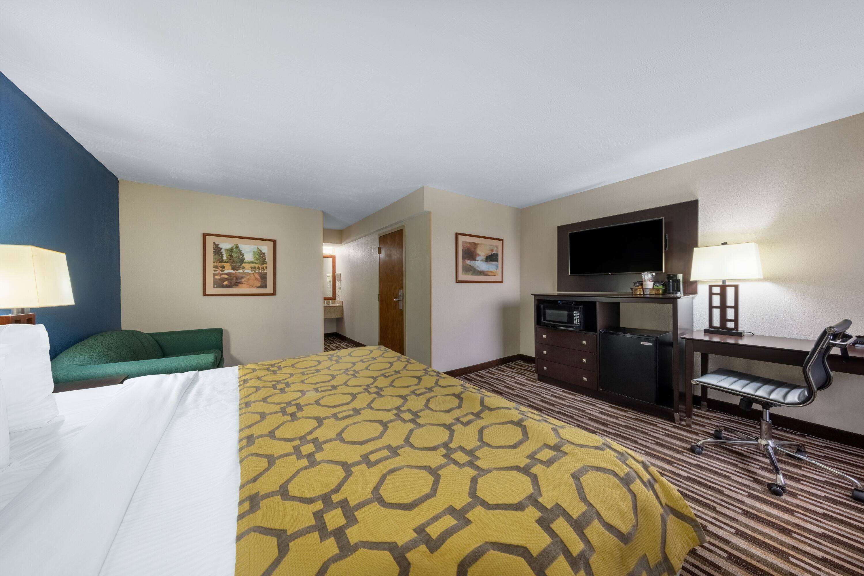 Una habitación de hotel con cama, escritorio, televisión y una kitchenette pequeña.