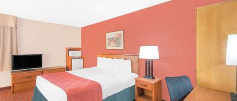 A hotel room with a bed, a TV, a desk, and a chair.