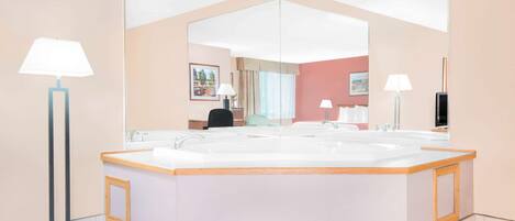 A modern bathroom with a large bathtub, a mirror, and two floor lamps.