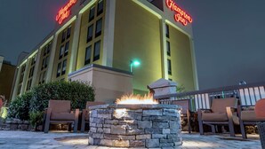 A Hampton Inn hotel exterior at night with a stone fire pit and outdoor seating.