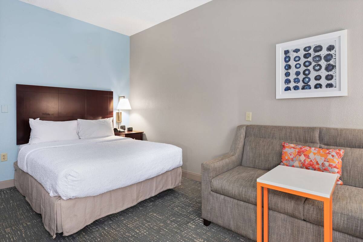 A hotel room with a bed, a sofa, a small table, and a framed picture on the wall.