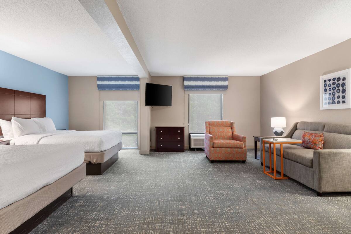 A hotel room with a large bed, a sofa, a chair, a TV, and a dresser.