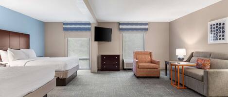 Habitación de hotel con una cama grande, un sofá, una silla, un televisor y un aparador.