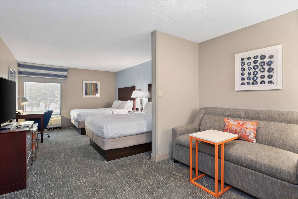 A hotel room with two beds, a sofa, a desk with a computer, and a TV.