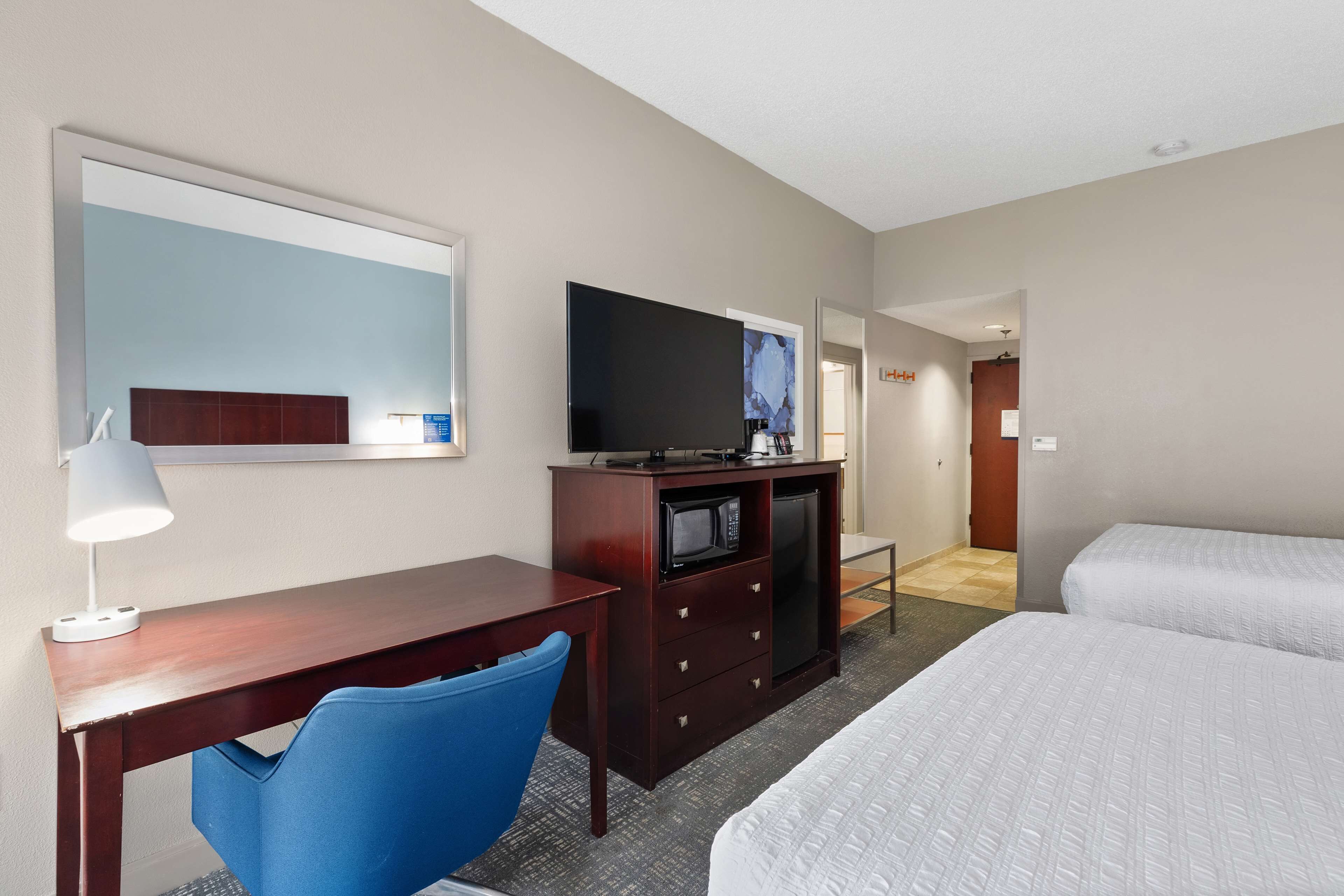 A hotel room with a desk, a chair, a television, a microwave, and two beds.