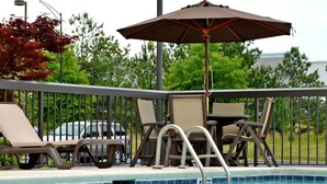 A poolside area with lounge chairs, a table, and an umbrella.