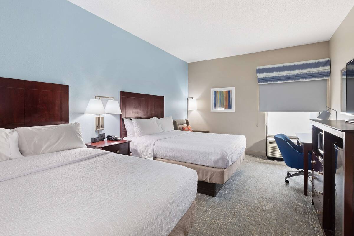A hotel room with two beds, a desk, a chair, and a TV.