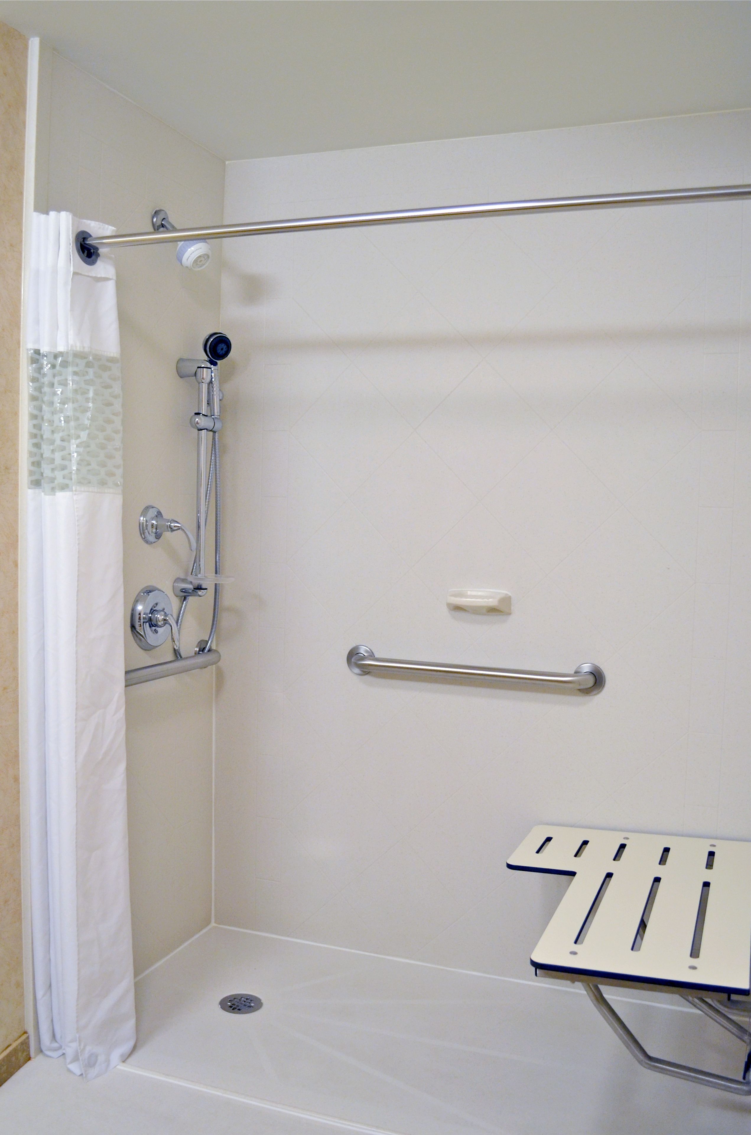 Eine barrierefreie Dusche mit Haltegriff, Duschkopf und einer kleinen Ablagefläche.