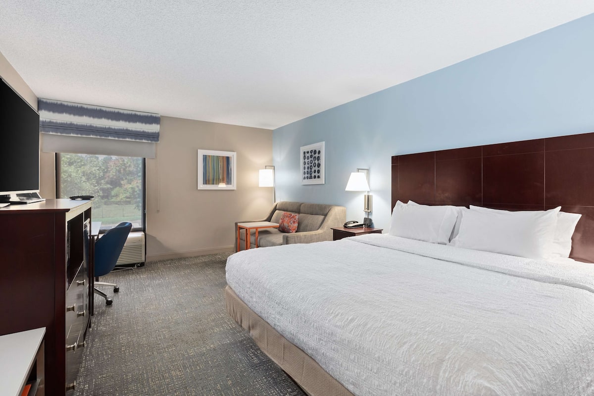 A hotel room with a large bed, a desk, a chair, and a window with a view.