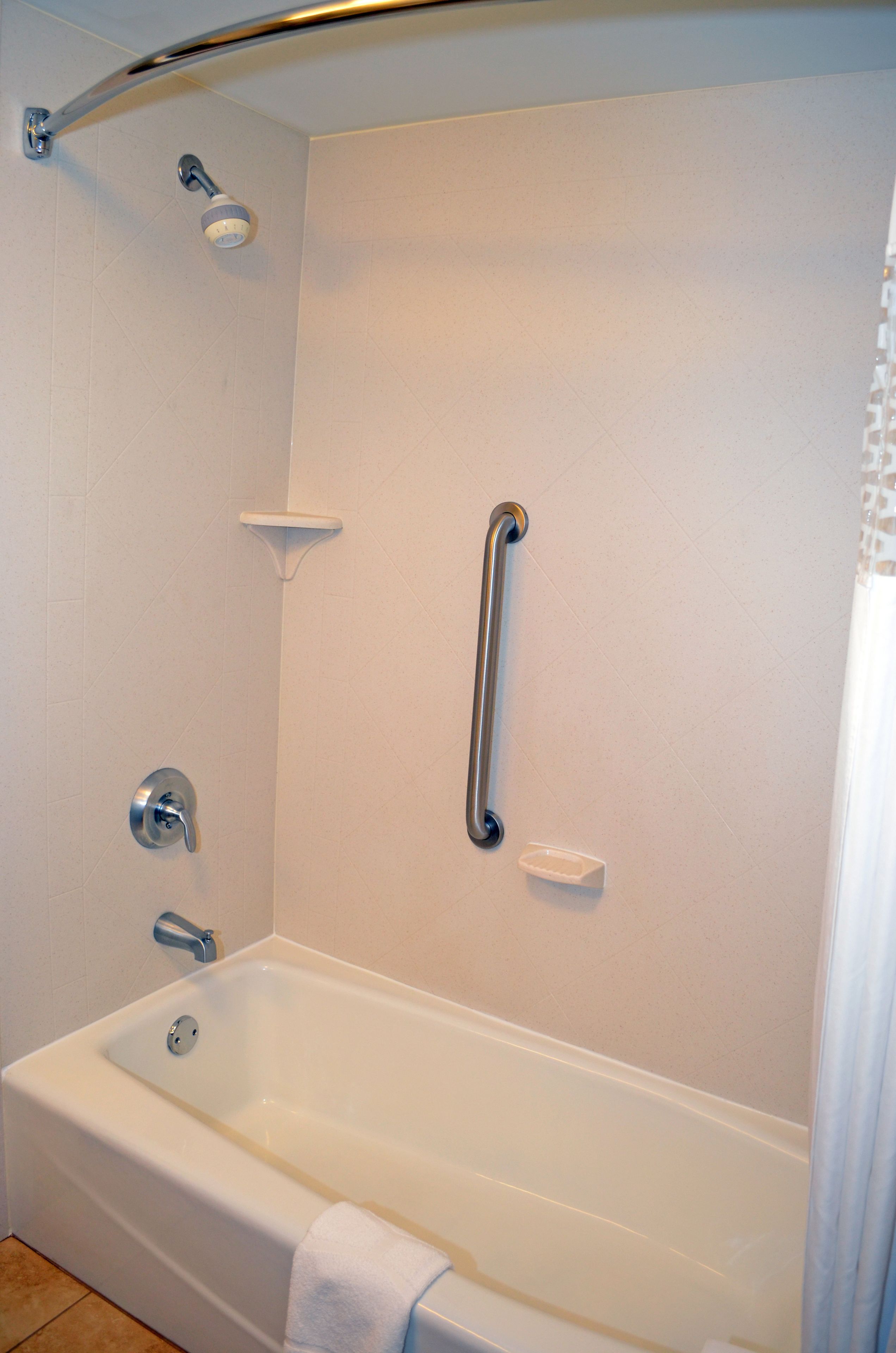 A white bathtub with a showerhead, grab bar, and a small shelf.