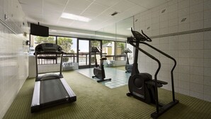 A gym with a treadmill, elliptical, and stationary bike, large windows with a view, and a tiled floor. - Super 8 by Wyndham Calhoun (Calhoun)