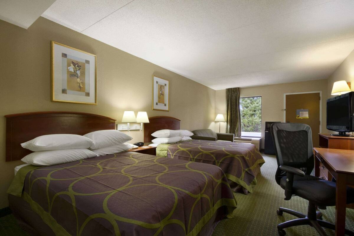 Quarto de hotel com duas camas, uma escrivaninha com computador e televisão.