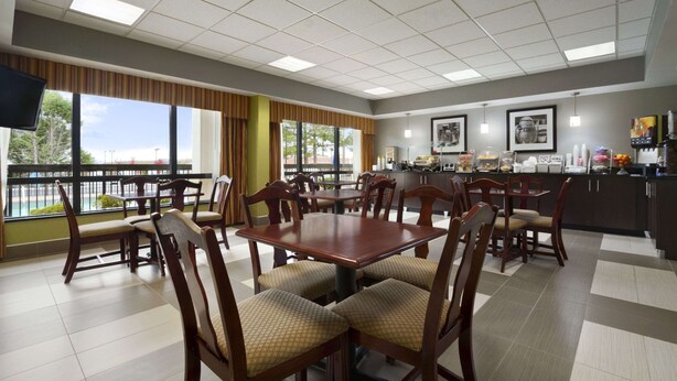 A dining area with multiple tables and chairs, a kitchen area with appliances, and large windows with a view. - Super 8 by Wyndham Calhoun (Calhoun)