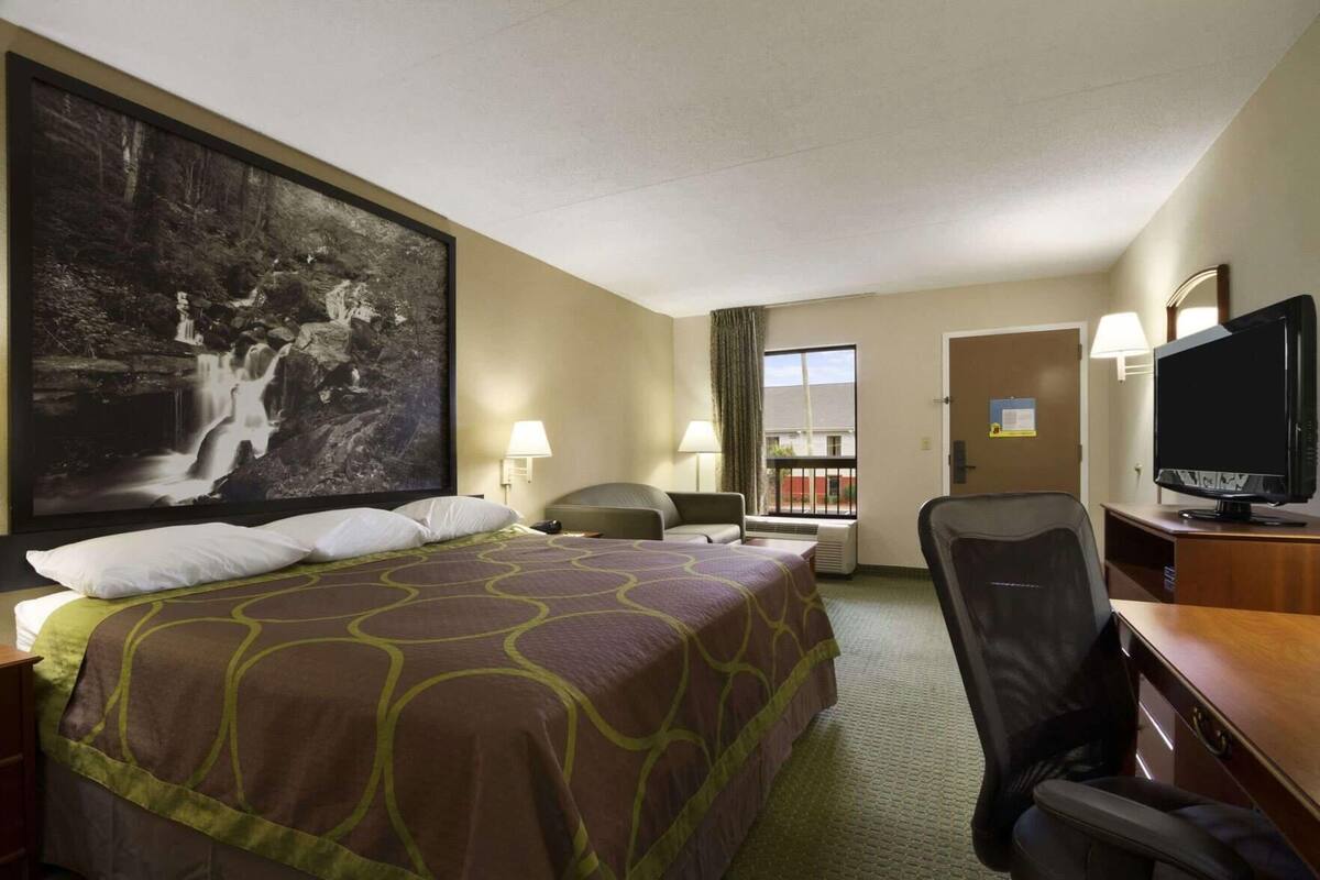 Quarto de hotel com uma cama grande, uma escrivaninha com televisão, uma cadeira e uma janela com vista para um edifício.