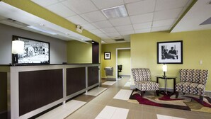 A reception area with a reception desk, two patterned chairs, a framed photo on the wall, and a tiled floor. - Super 8 by Wyndham Calhoun (Calhoun)