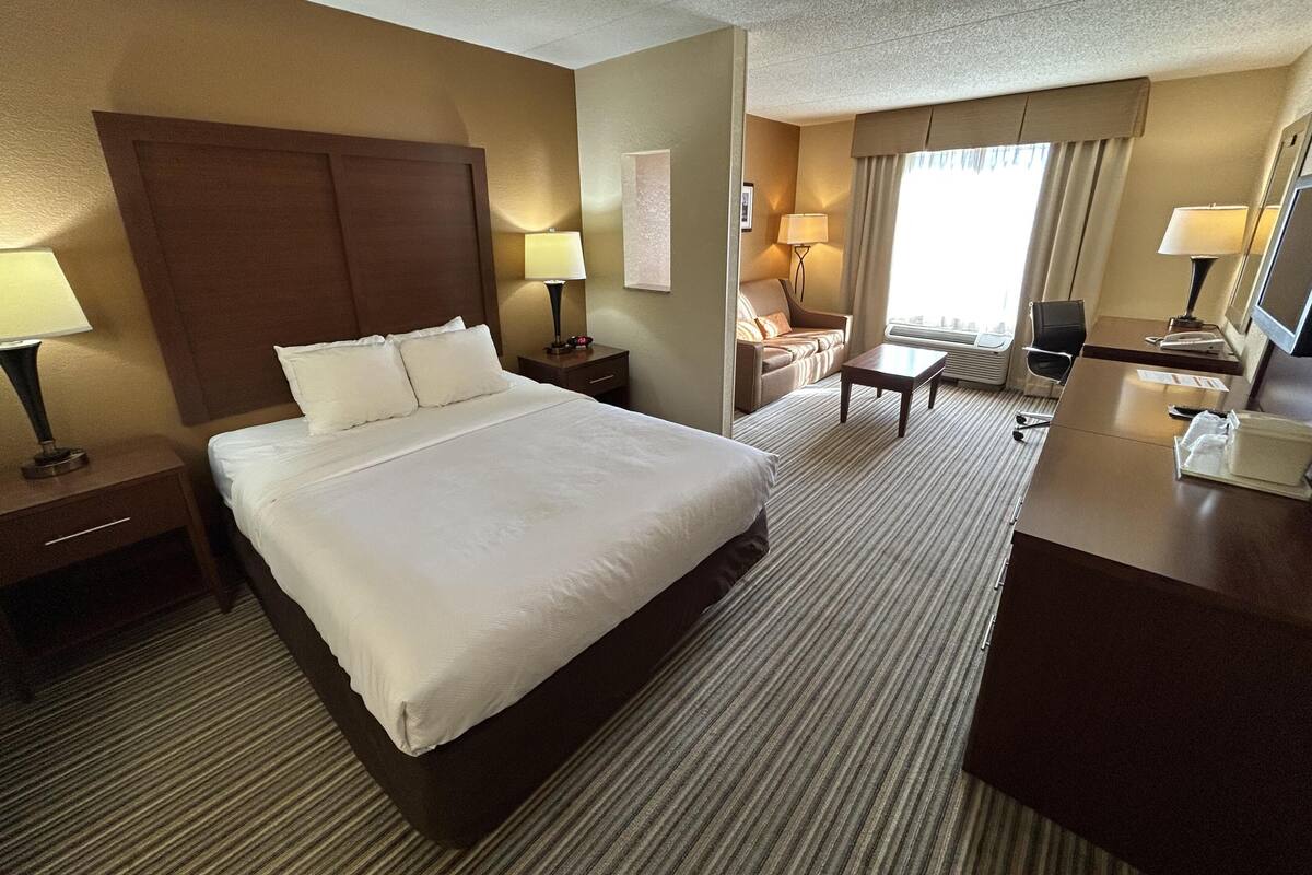A hotel room with a large bed, a desk, a chair, a sofa, and a TV.