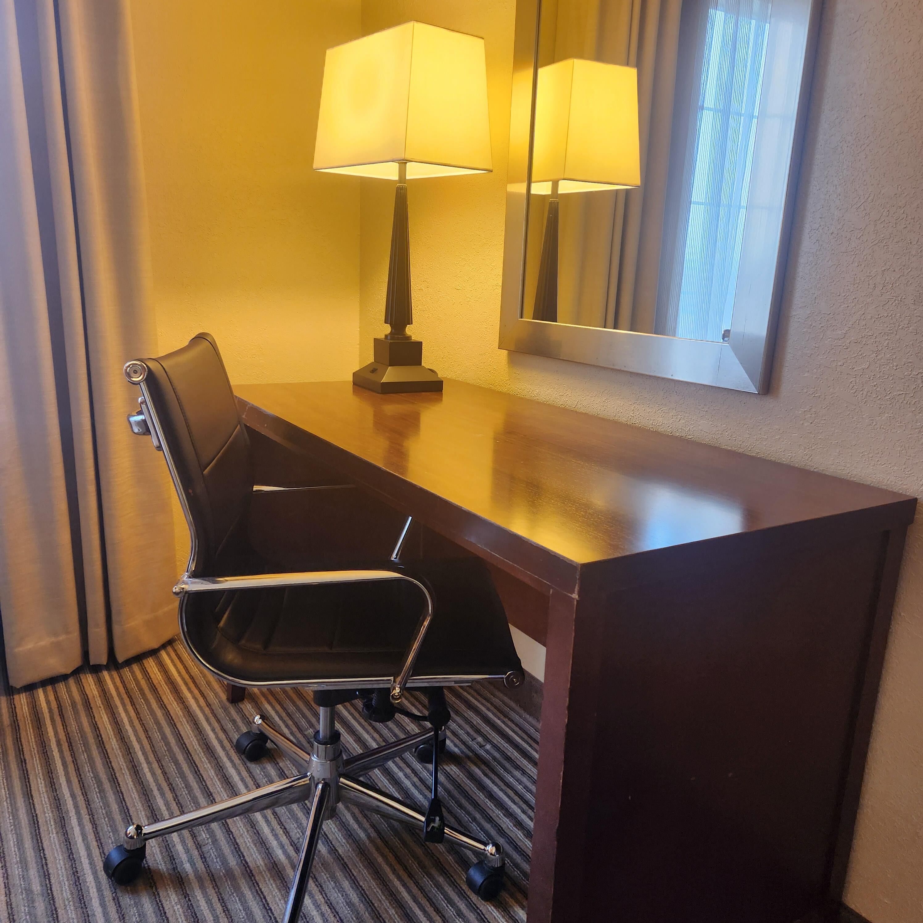 Un escritorio de hotel con una silla, una lámpara y un espejo.
