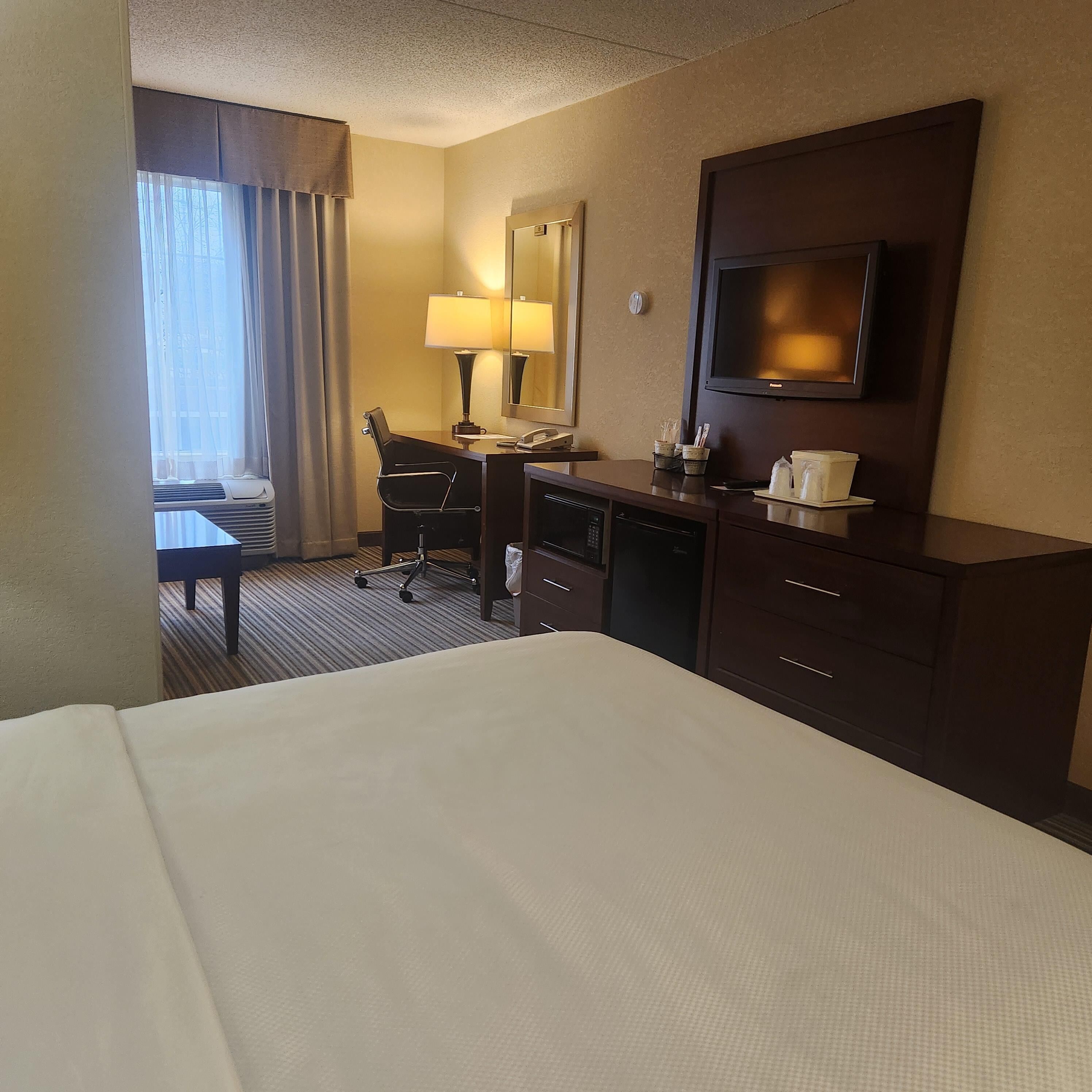 Habitación de hotel con cama, escritorio, silla, televisión y ventana con cortinas.
