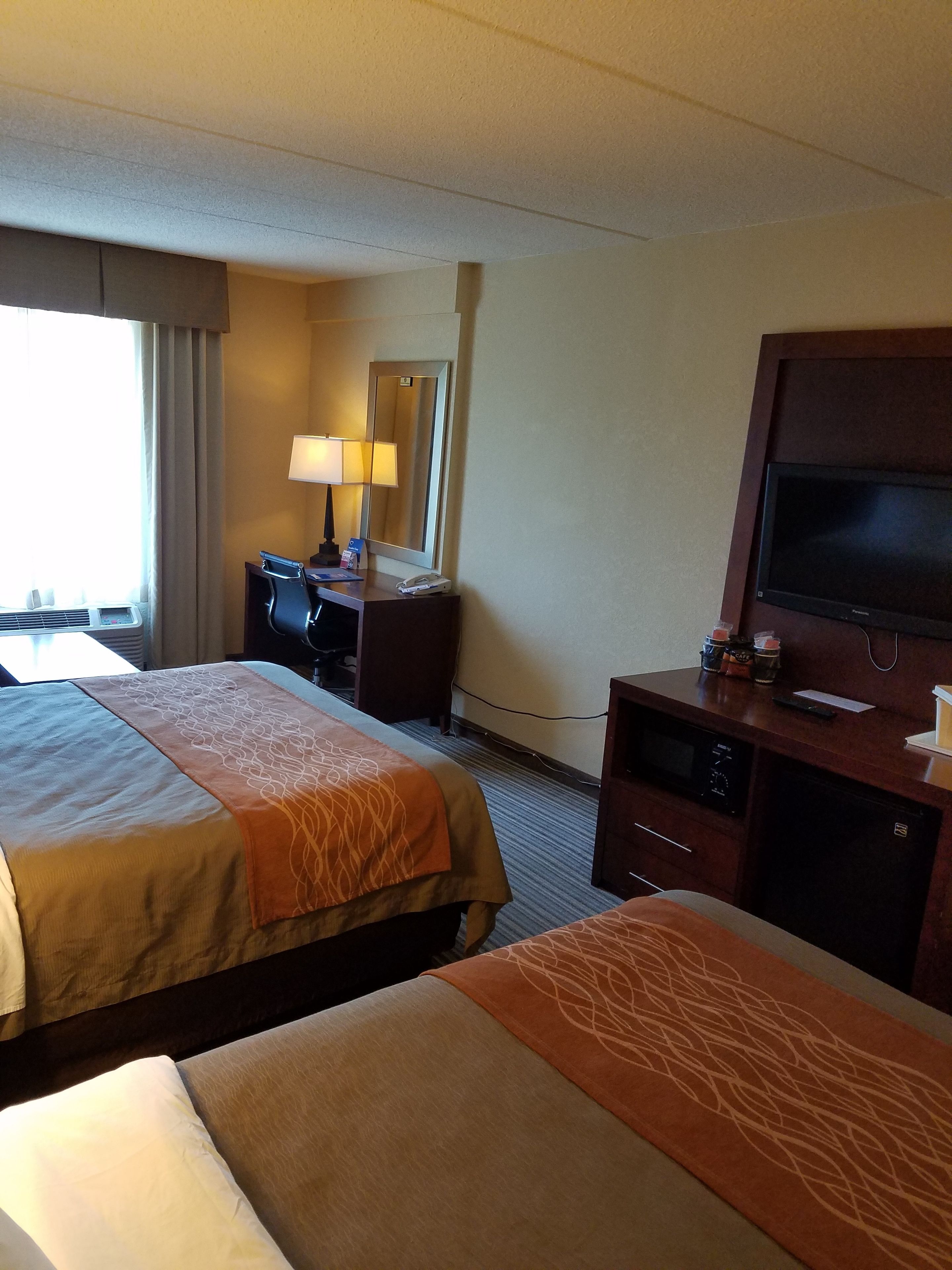 A hotel room with two beds, a desk, a television, and a window with curtains.
