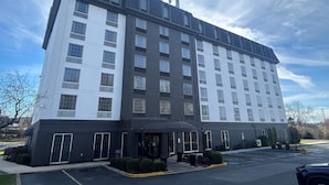 A multi-story hotel with a modern design, featuring a mix of white and dark grey exterior walls, large windows, and a covered entrance area with a small garden. - Best Western Chocolate Inn at the Park (Hummelstown)