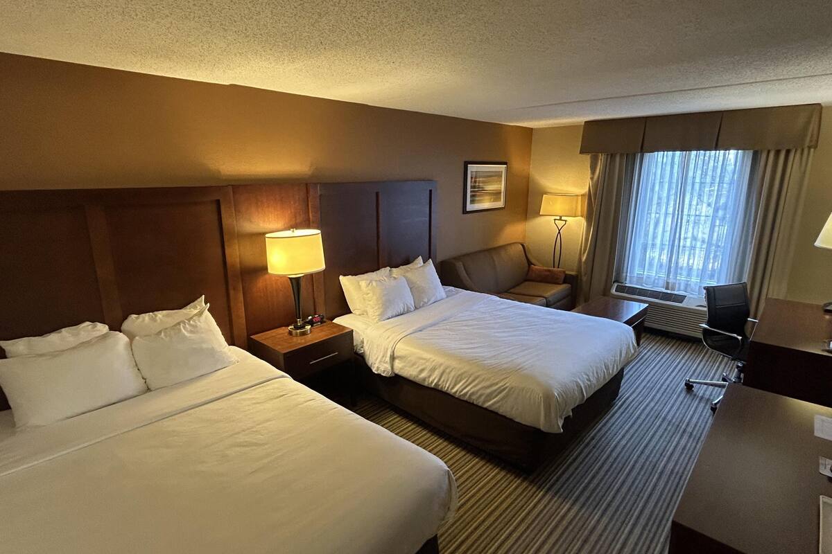 A hotel room with two beds, a desk, a chair, a lamp, and a window with curtains.