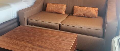Habitación de hotel con sofá cama, una mesita de madera y un cuadro en la pared.