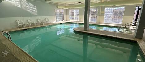 An indoor swimming pool with clear water, surrounded by white walls and windows.