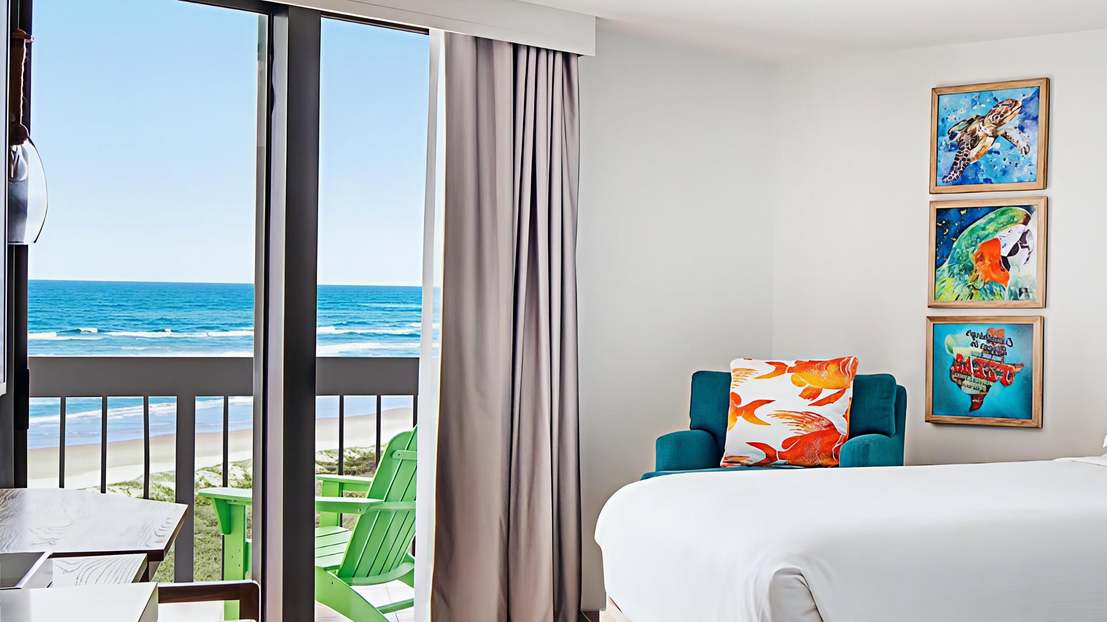 A hotel room with a bed, a chair, a table, and a view of the ocean.
