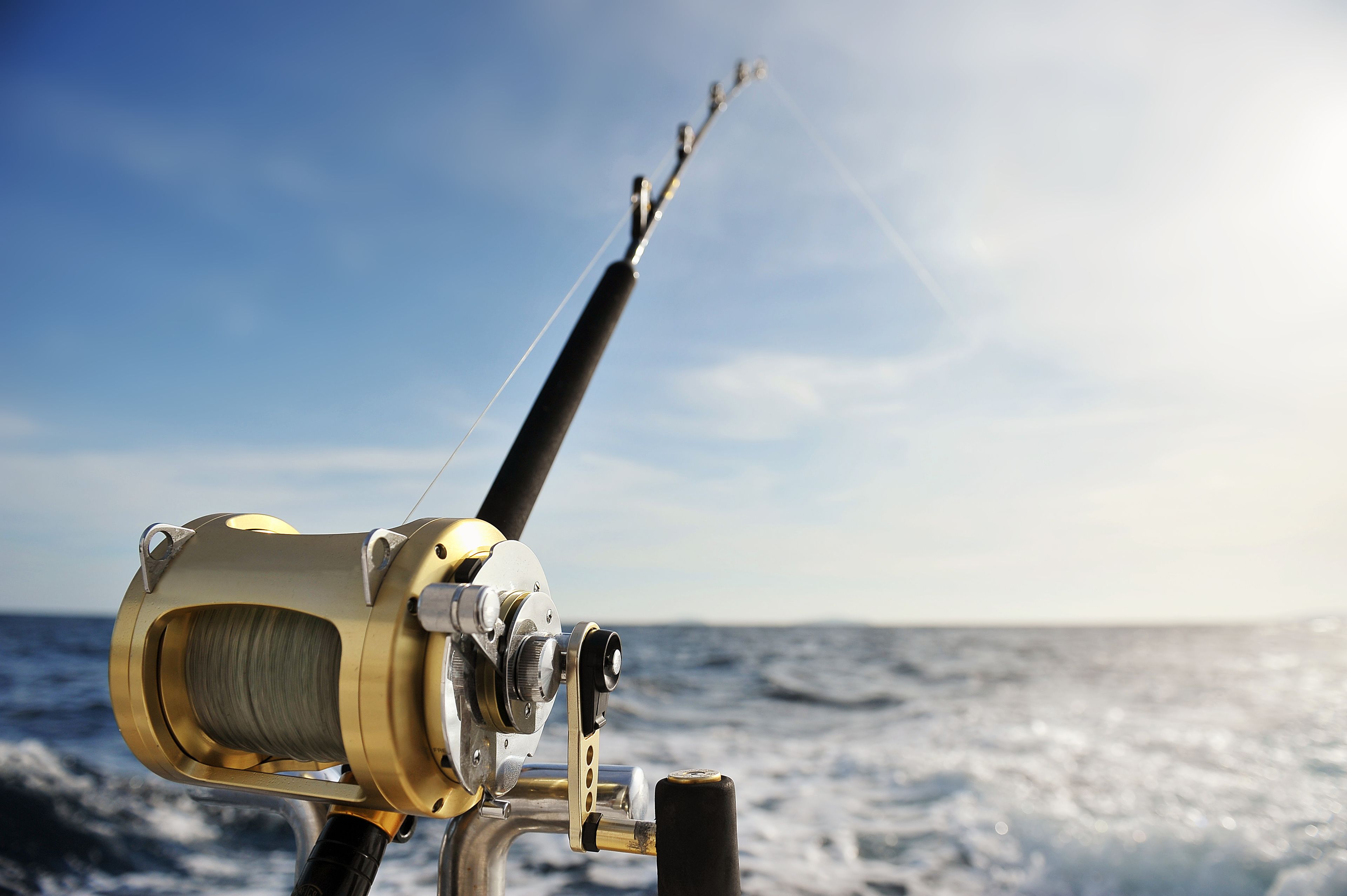 A fishing rod with a reel on a boat, with the ocean in the background.