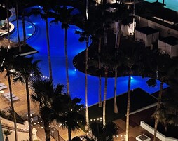Vista aérea de un resort con una amplia piscina rodeada de palmeras y una terraza bien iluminada.