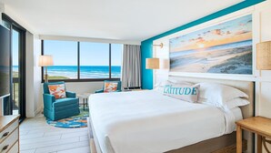 Habitación de hotel con una cama grande, vista al océano, un cuadro de una playa y una pared de acento azul.