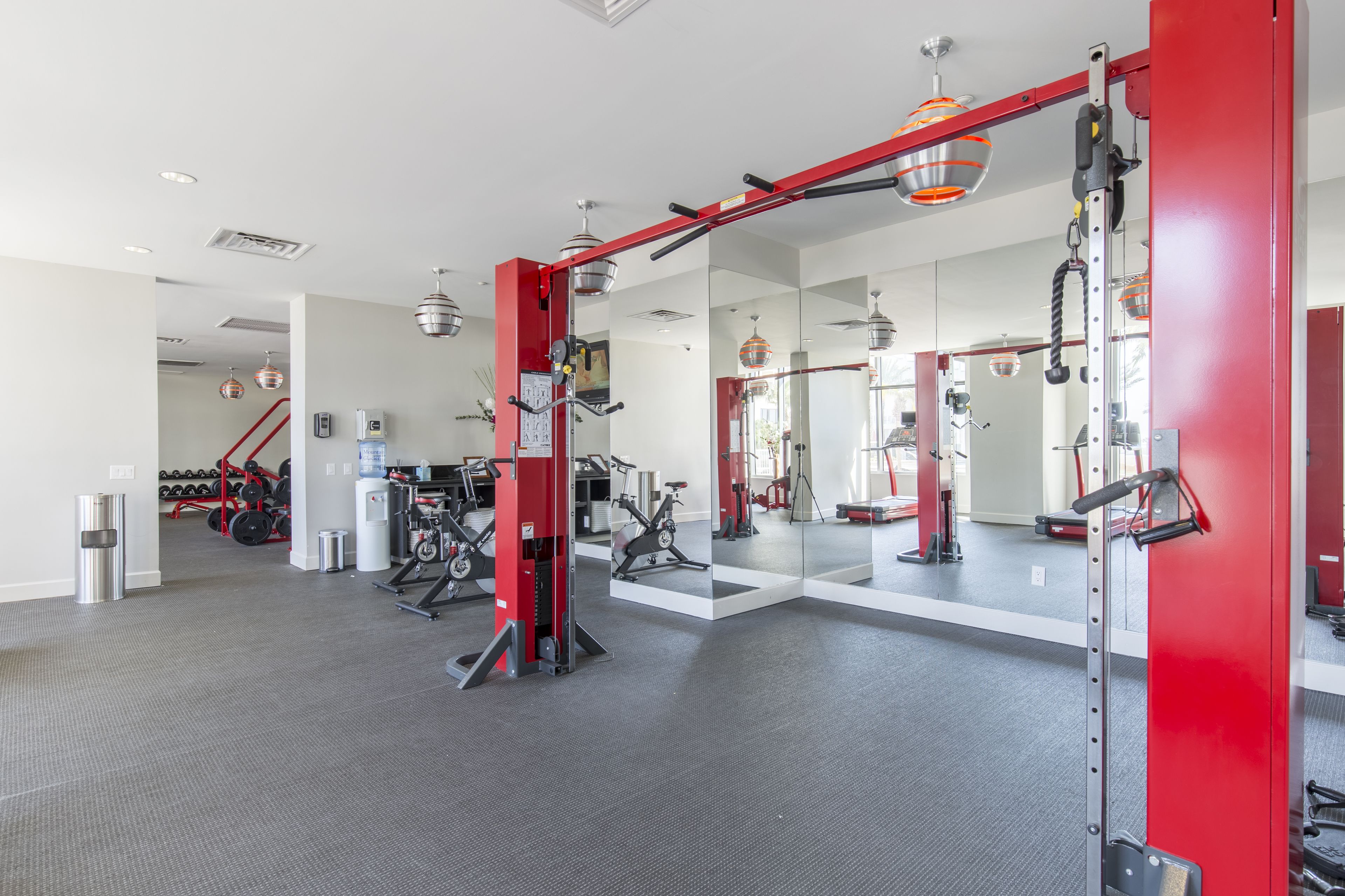 Ein modernes Fitnessstudio mit roter Ausstattung, einem großen Spiegel und einem aufgeräumten, geräumigen Layout.